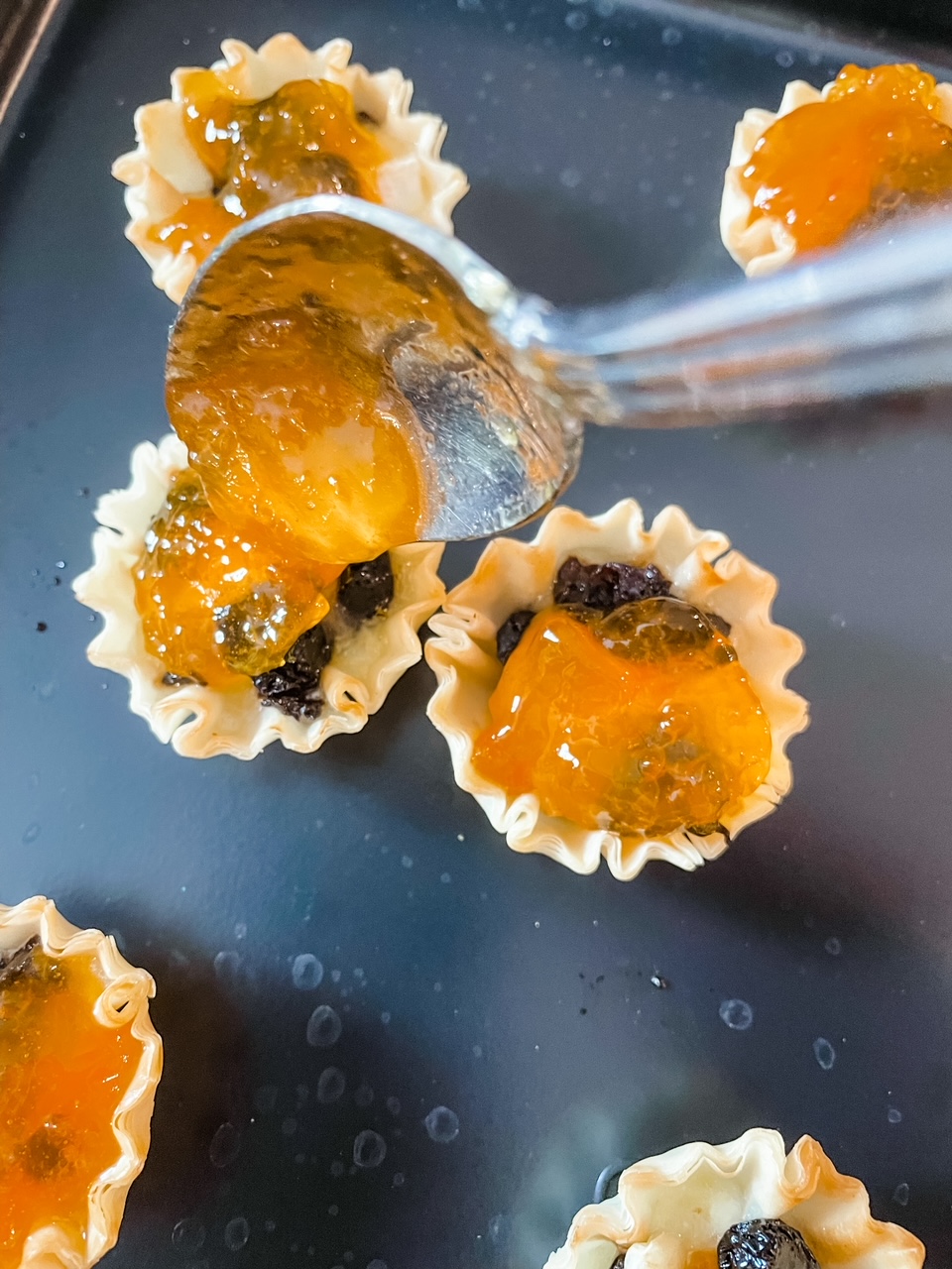 A spoon putting apricot preserves into the tarts