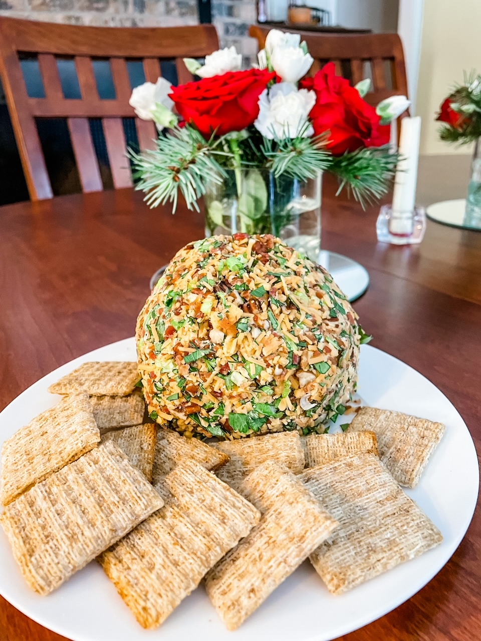 The finished Best Holiday Cheese Ball with crackers and a bouquet of flowers behind it.
