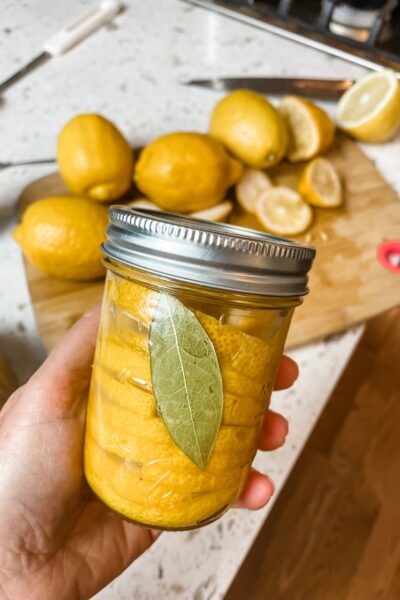 Marie holding the DIY Preserved Lemons in a jar above the counter with the ingredients