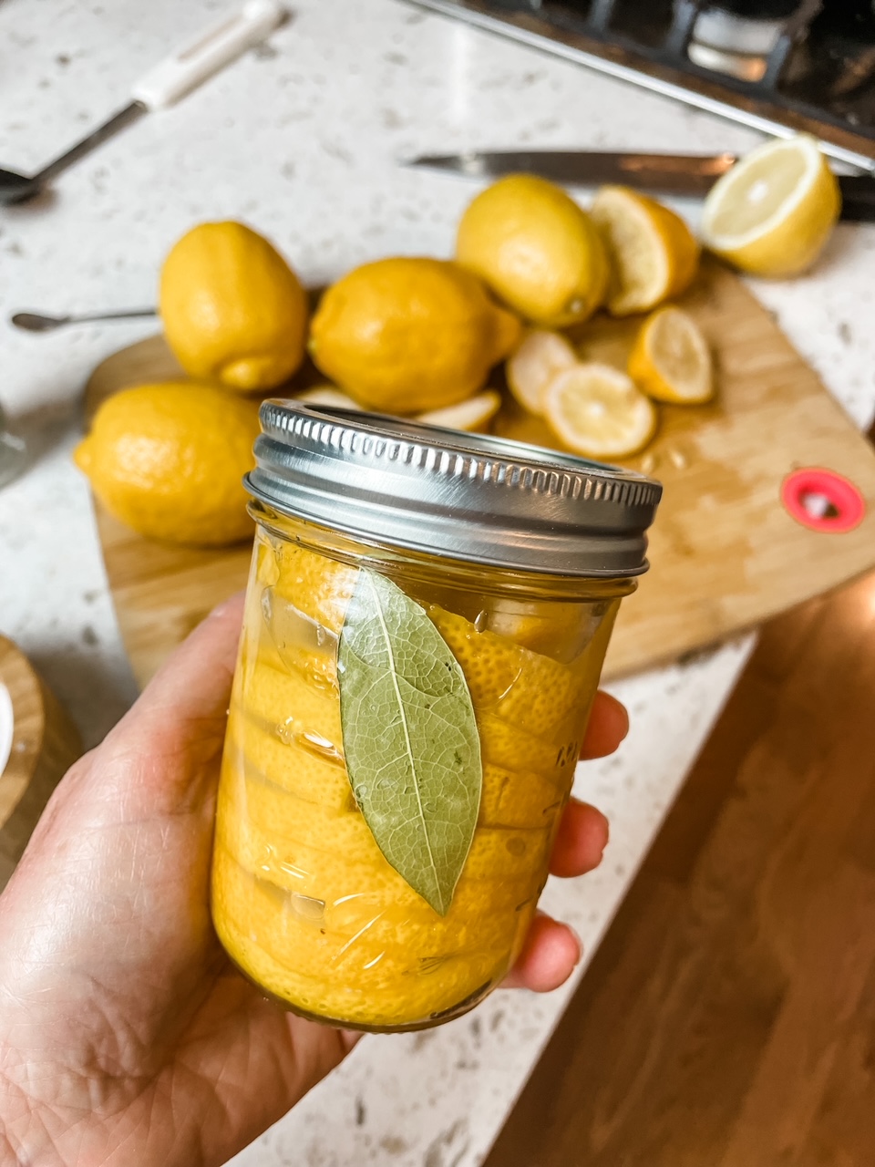 Marie holding the DIY Preserved Lemons in a jar above the counter with the ingredients
