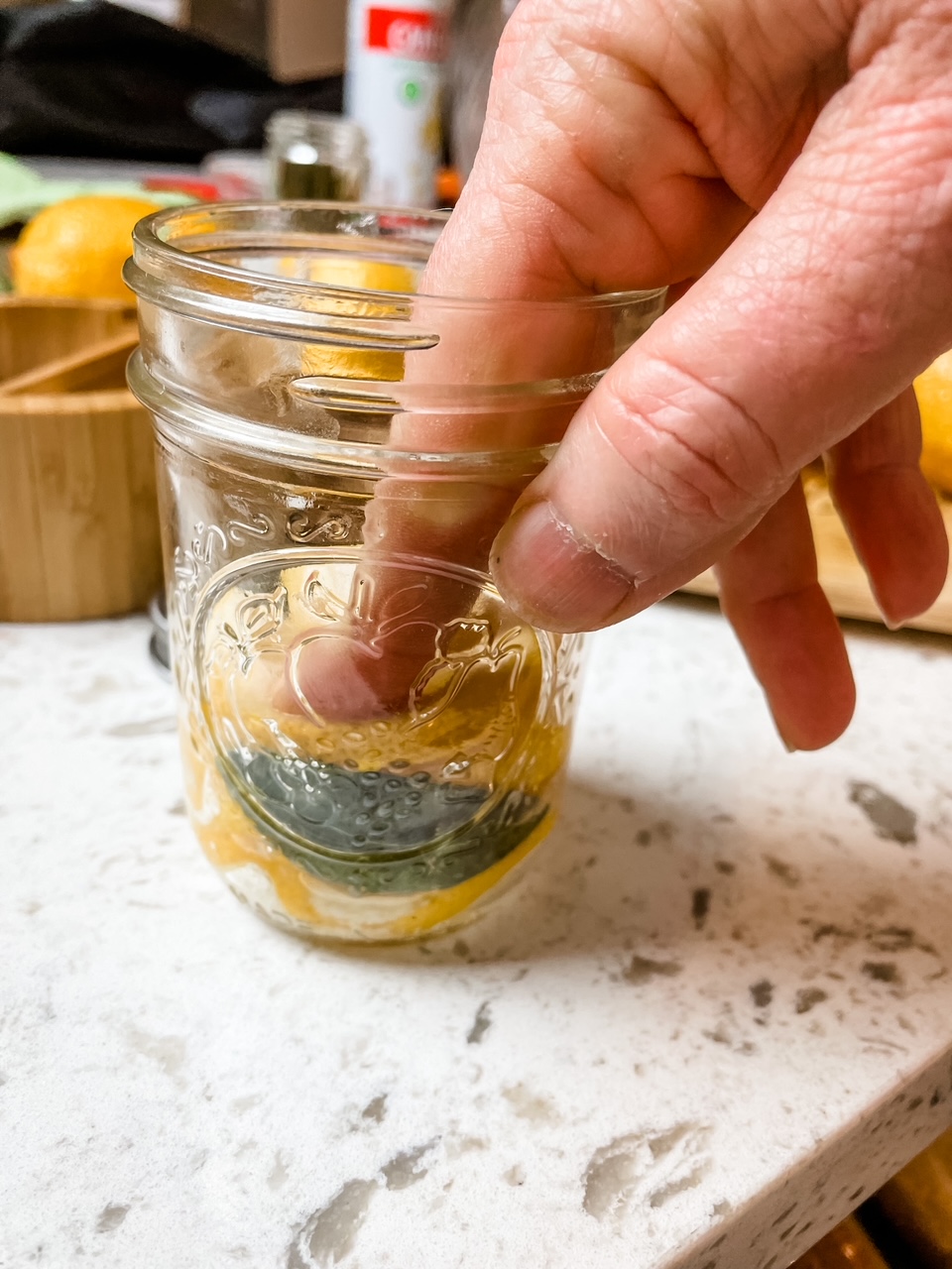 Marie using her hands to firmly press down the lemon slice layer into the jar