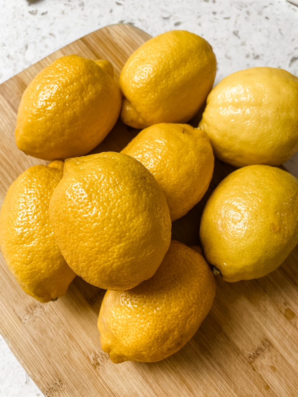 A pile of lemons on top of a wooden cutting board