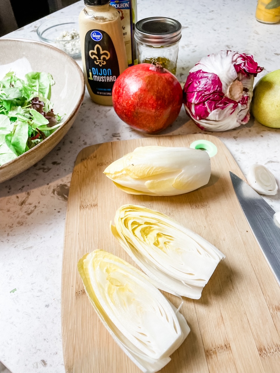 Some of the sliced endives ona wooden cutting board, with a pomegranate behind them