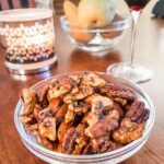 A bowl of the Rosemary Maple Spiced Nuts on a table next to a candle