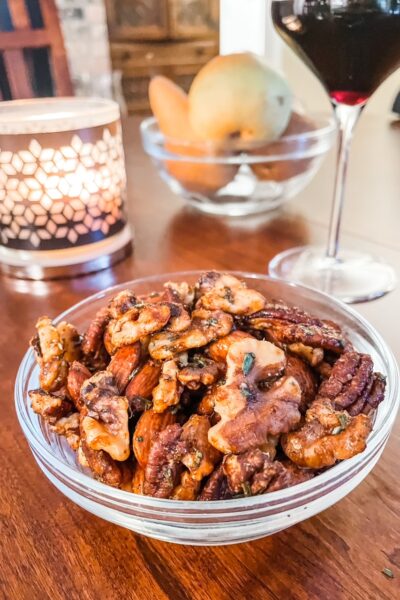 A bowl of the Rosemary Maple Spiced Nuts on a table next to a candle