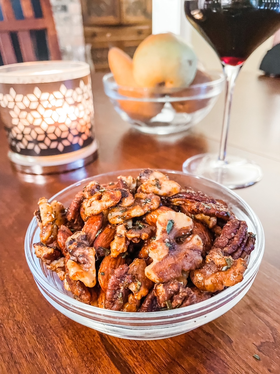 A bowl of the Rosemary Maple Spiced Nuts on a table next to a candle
