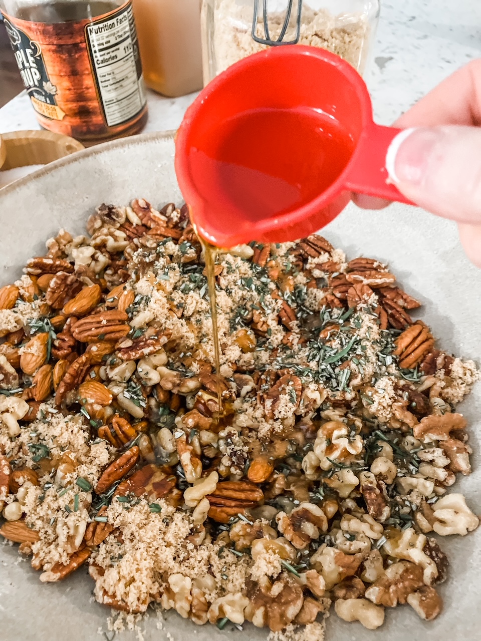 A bowl with the nut mixture and the maple syrup being poured over