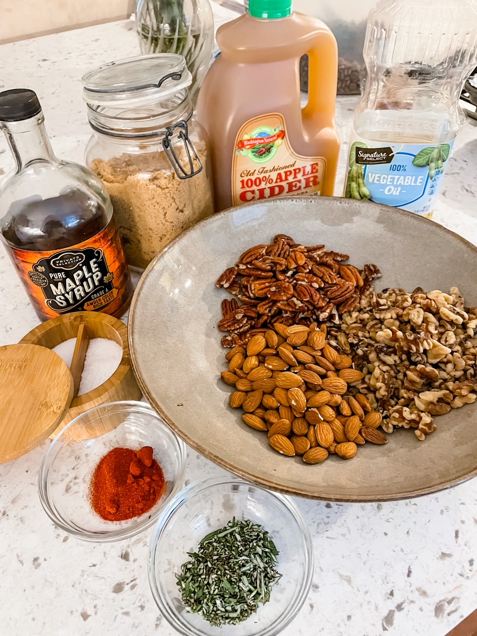 The ingredients for the Rosemary Maple Spiced Nuts - the nut mix, maple syrup, and spices on a counter