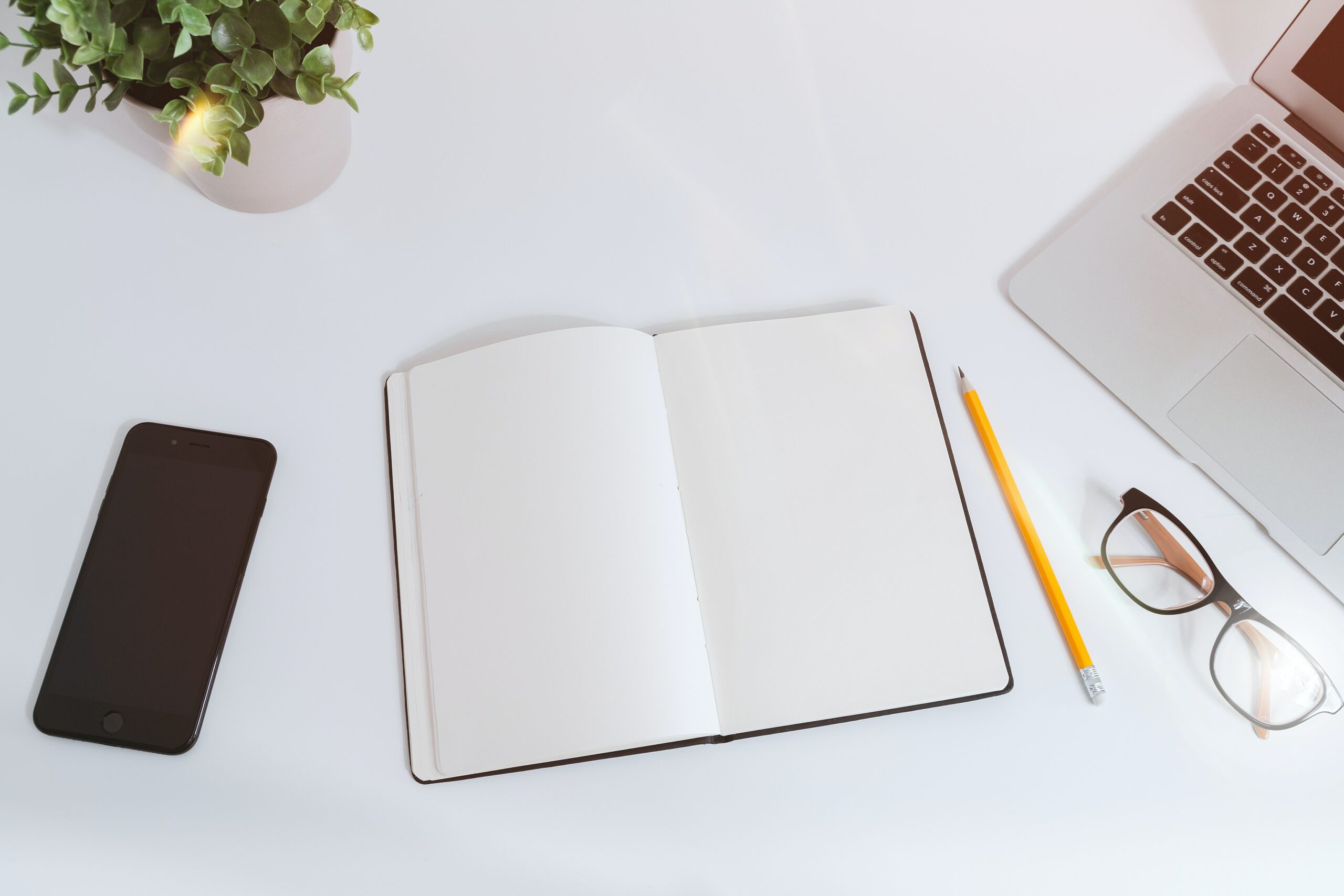 A desk with a phone, laptop, and notebook opened to a blank page