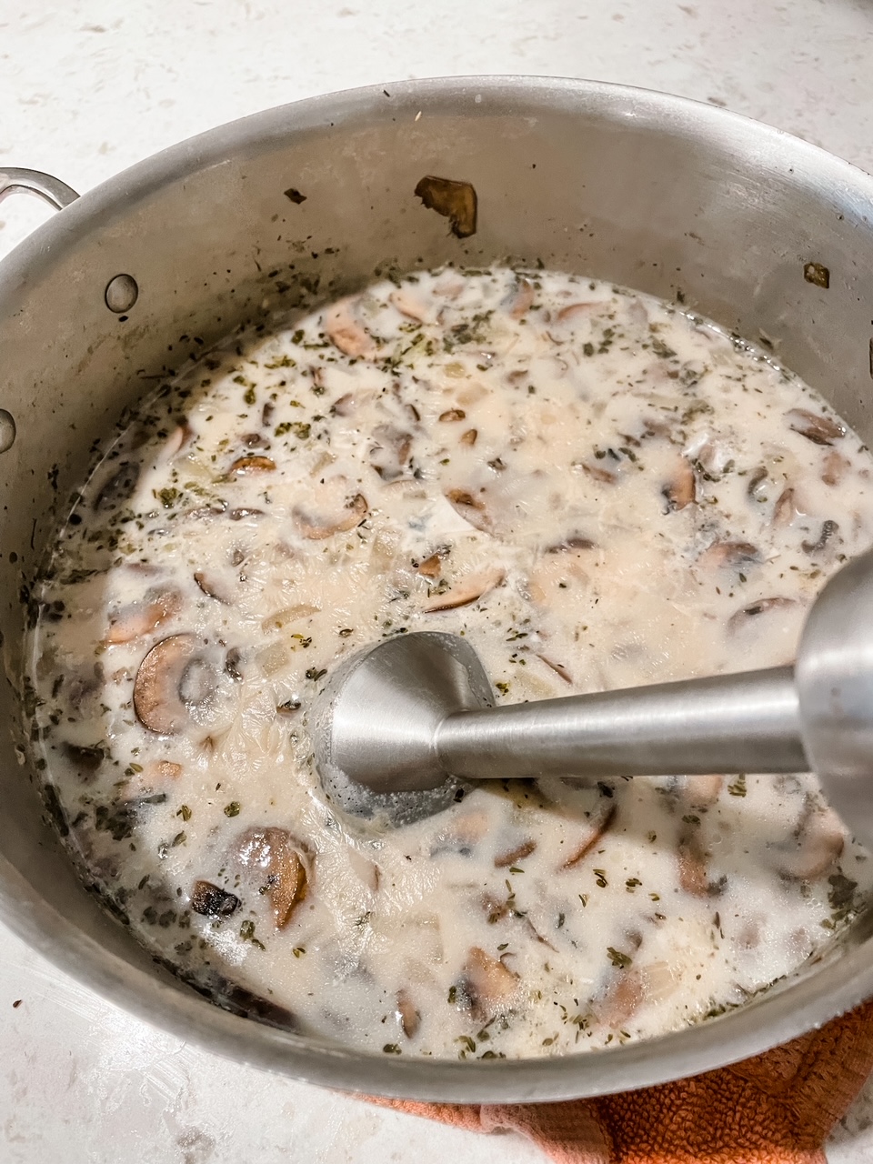 An immersion blender mixing together the mushrooms and broth base 