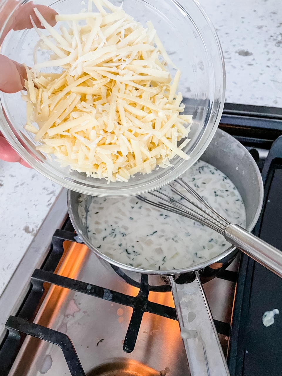 Shredded gruyere cheese being poured into the sauce mixture
