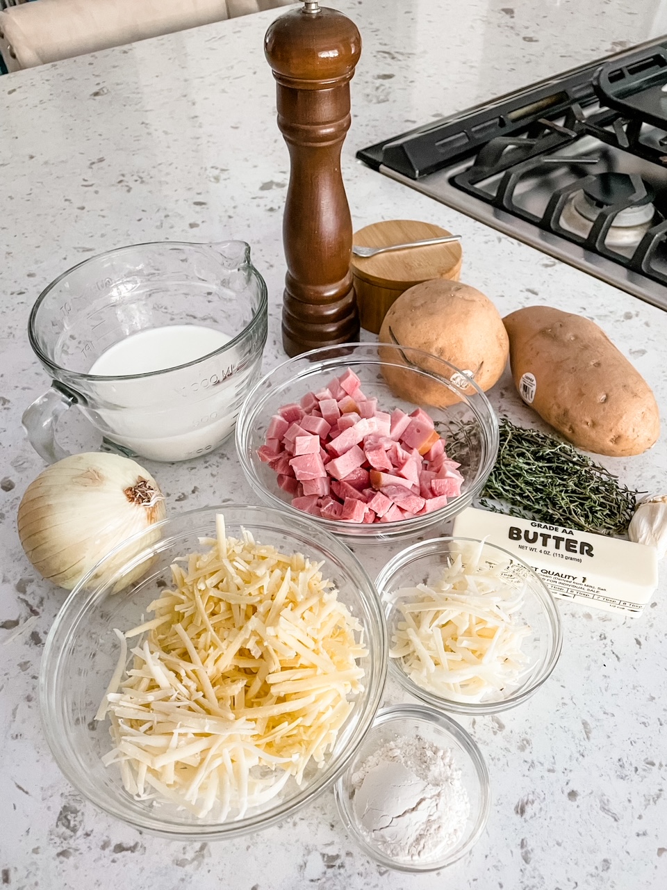 The ingredients laid out on a countertop - onion, salt, pepper, cheese, ham, potatoes, and thyme