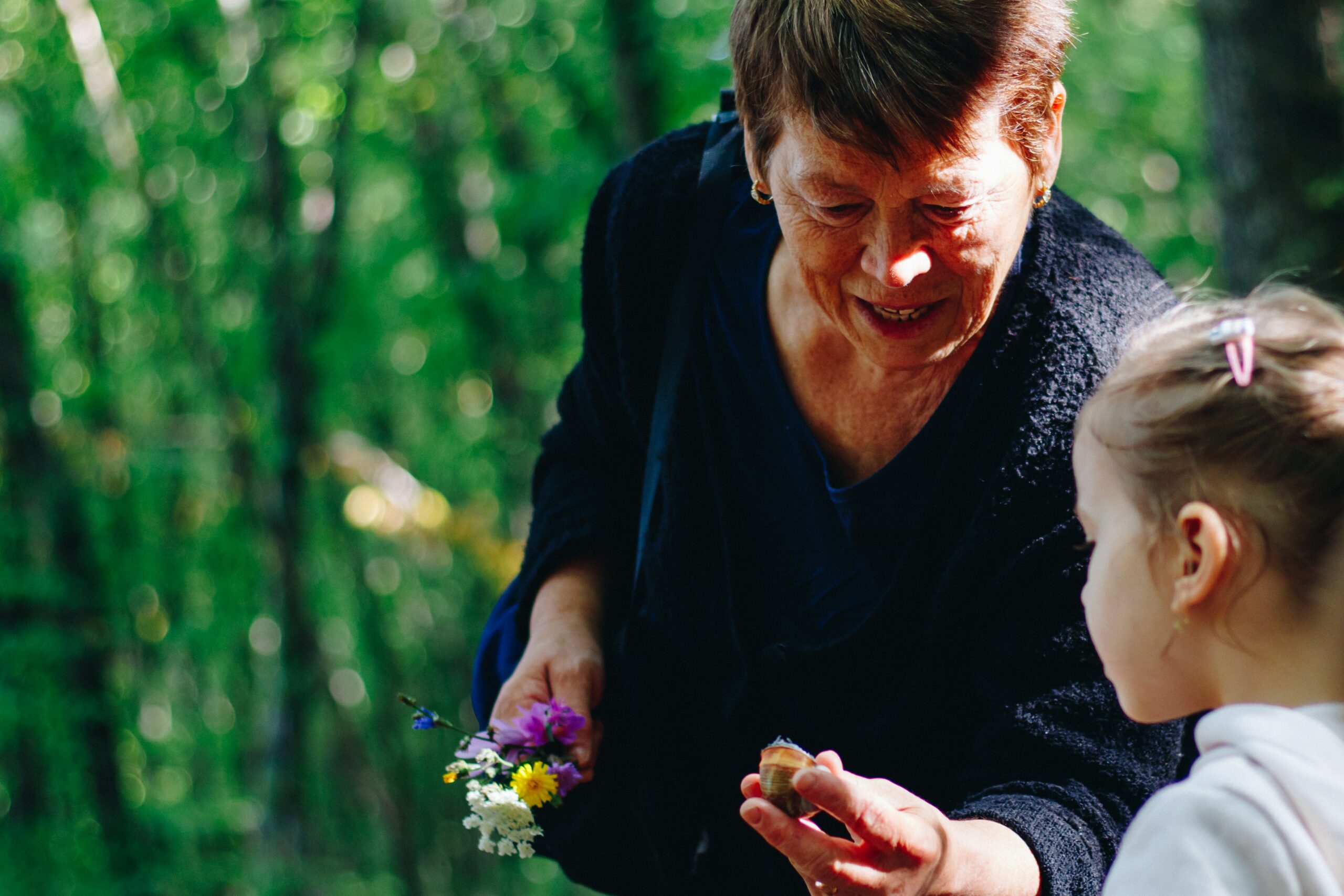 A grandmother showing a snail to her grandchild during a hike