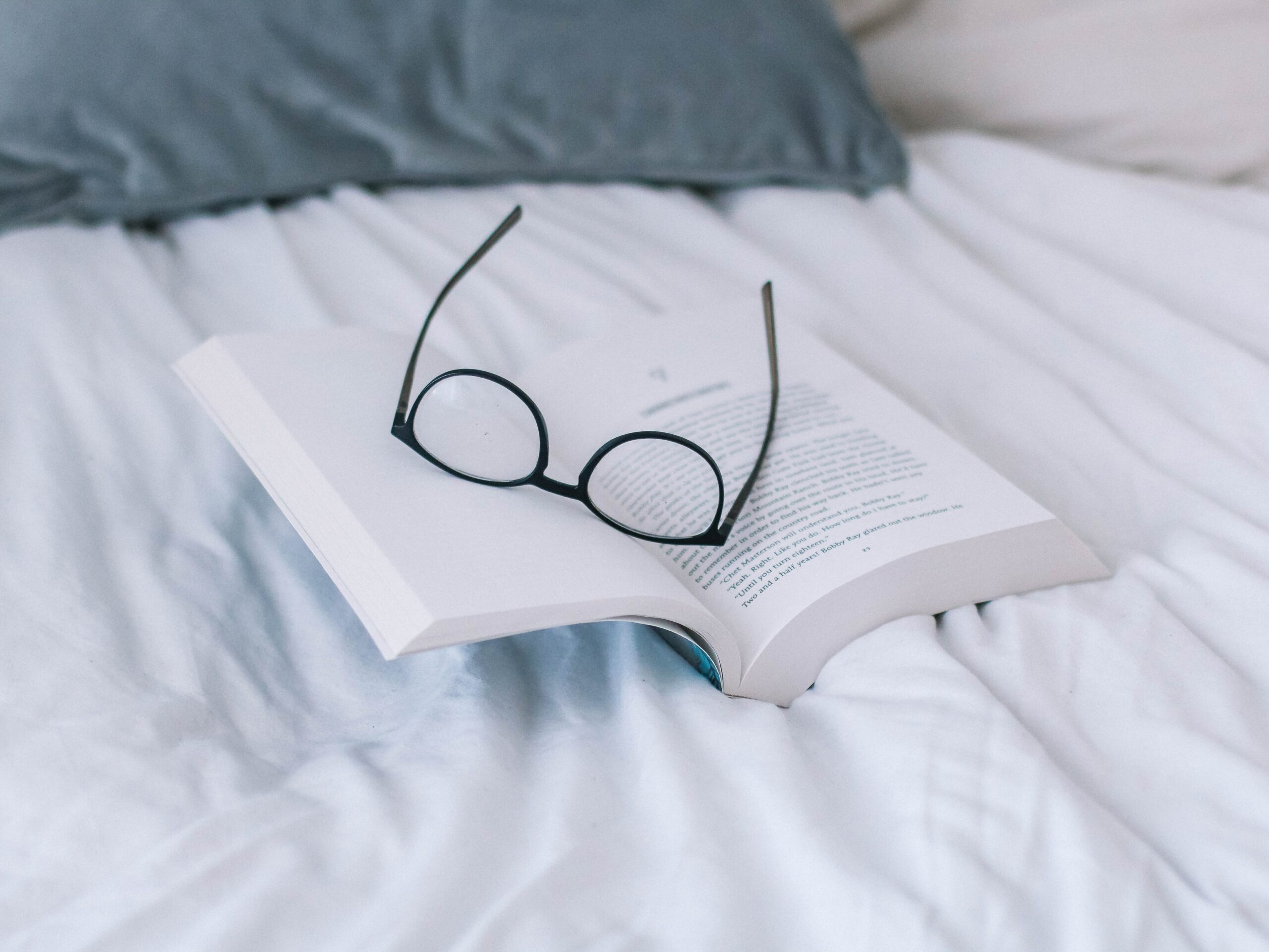 A bed with a book and a pair glasses