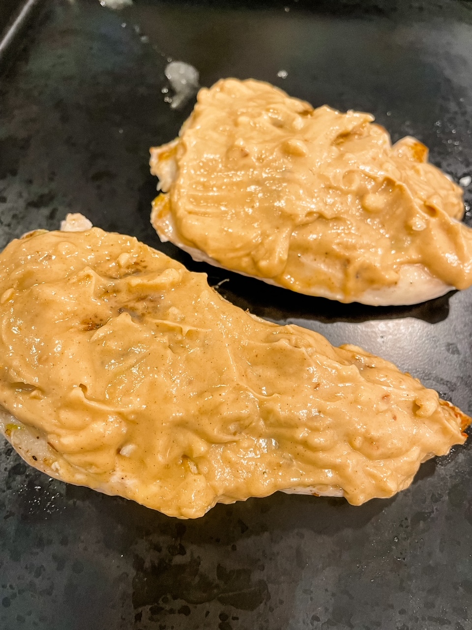 Two chicken breasts topped with the peanut mixture prior to cooking