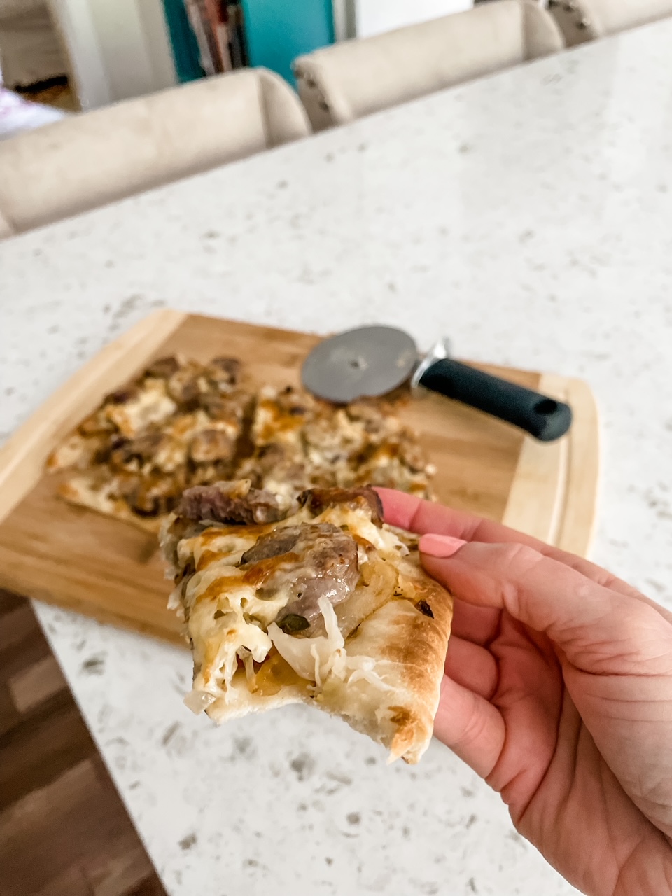 A hand holding up a slice of the Sausage, Sauerkraut and Gouda Flatbread with the rest in the background