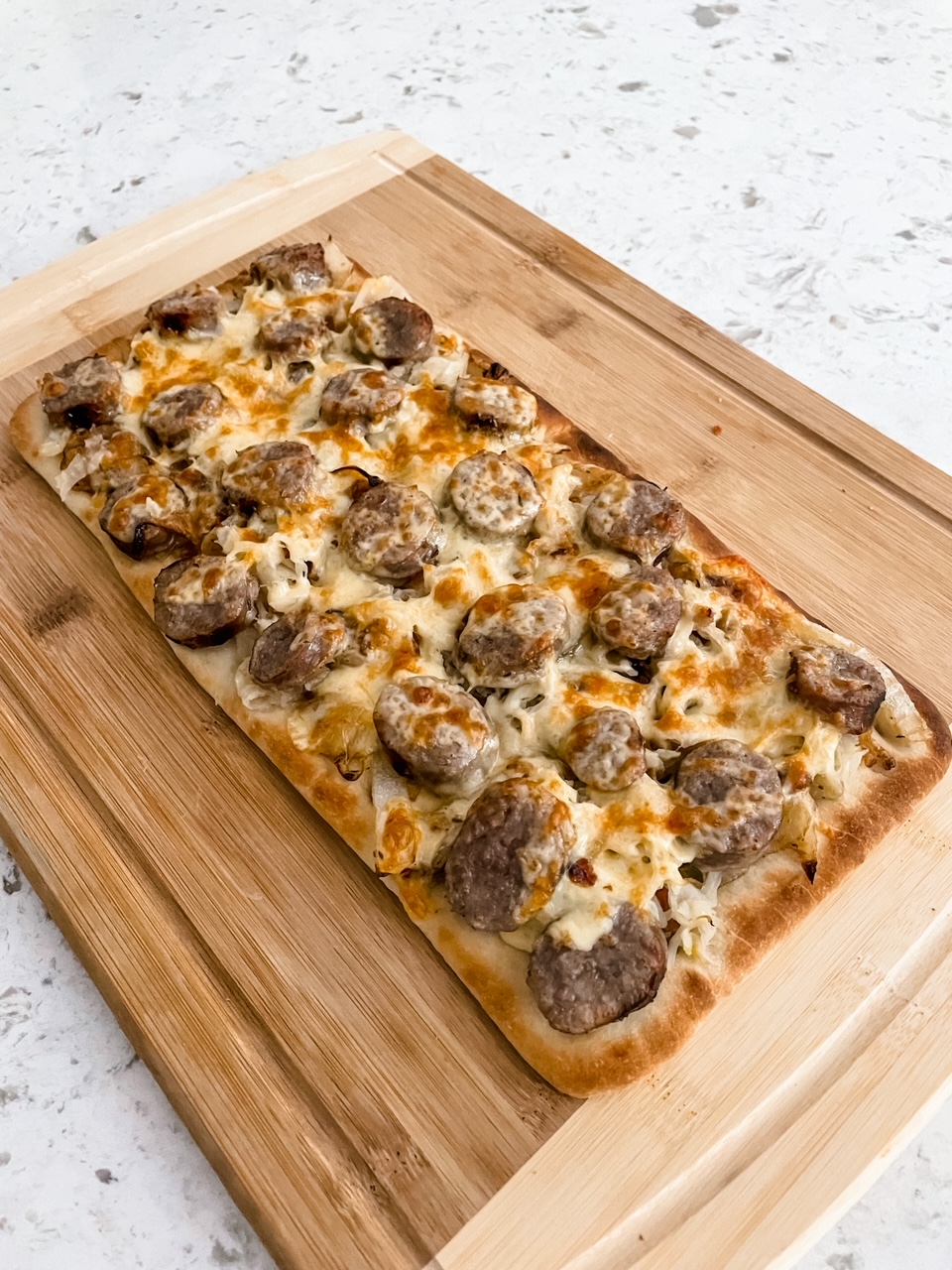 The finished Sausage, Sauerkraut and Gouda Flatbread cooling on a wooden cutting board