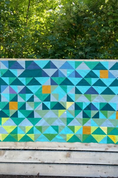 The partially finished temperature quilt update hanging off a wooden fence