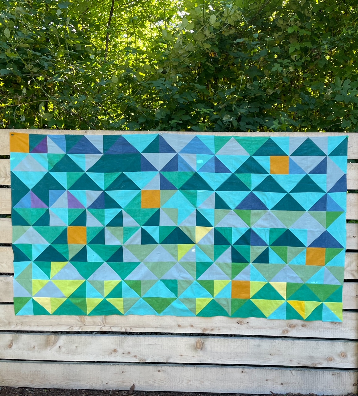 The partially finished temperature quilt update hanging off a wooden fence