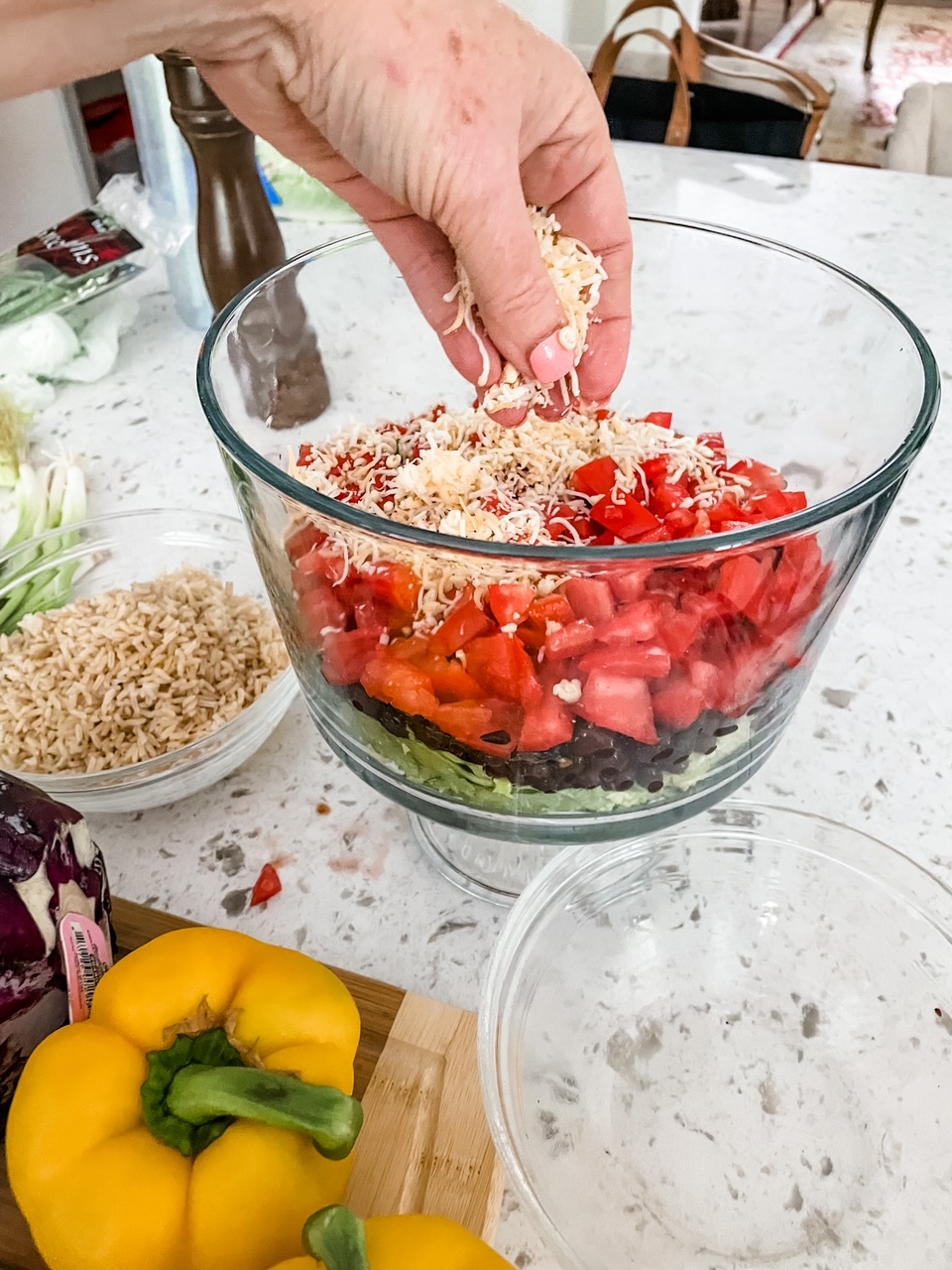 A hand adding ingredients to the trifle bowl in a layered pattern