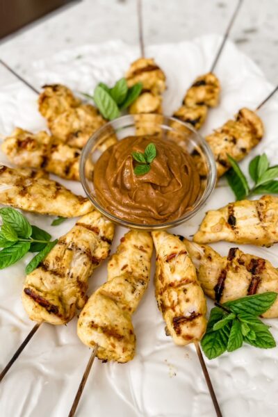 The finished Asian Chicken Skewers with Peanut Dipping Sauce on a plate with green garnish