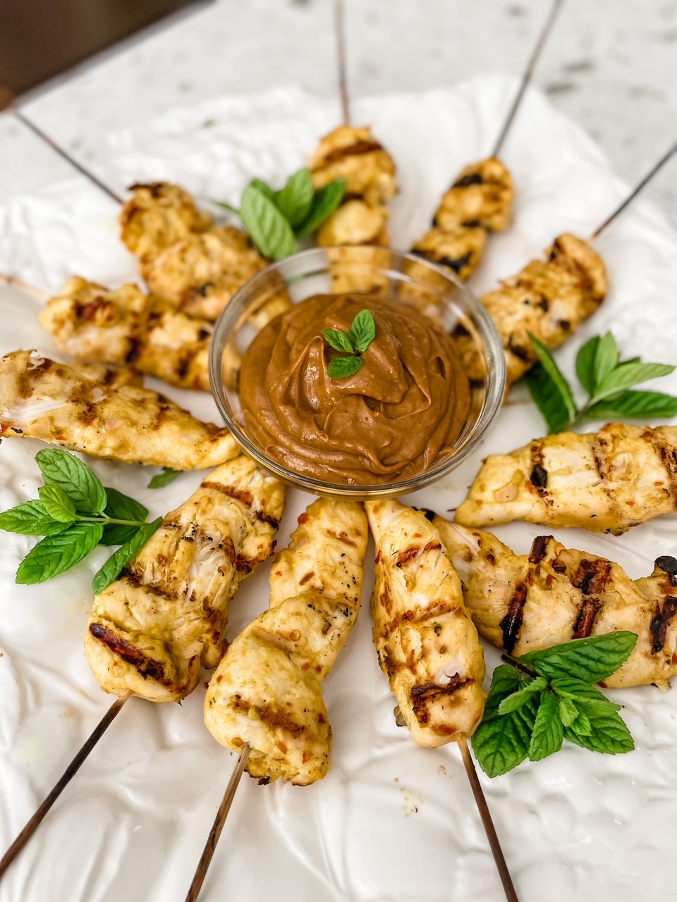 The finished Asian Chicken Skewers with Peanut Dipping Sauce on a plate with green garnish