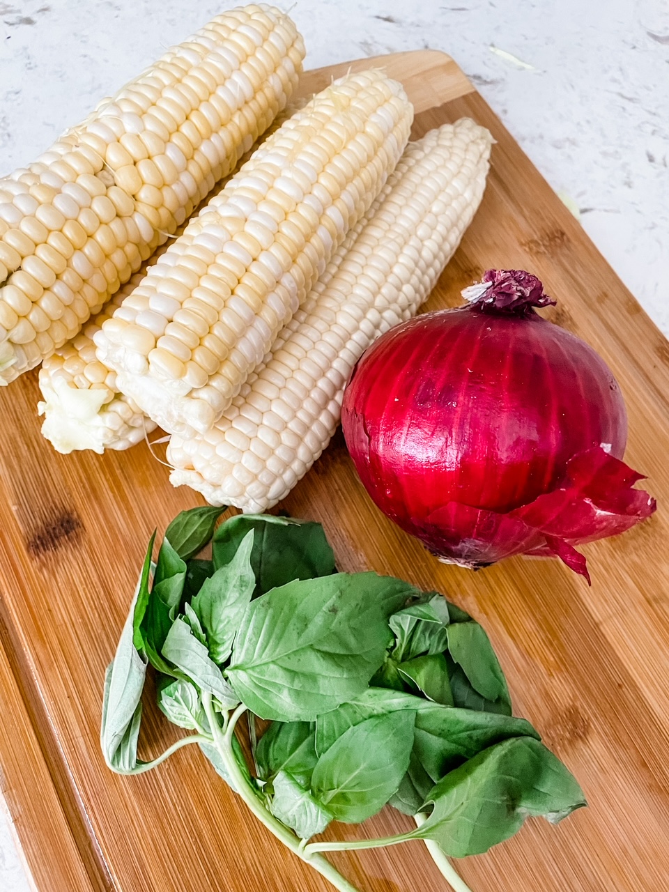 A few of the ingredients for Barefoot Contessa’s BEST Corn and Basil Salad - red onion, corn and basil