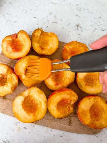 A brush brushing on oil onto sliced peaches for grilling