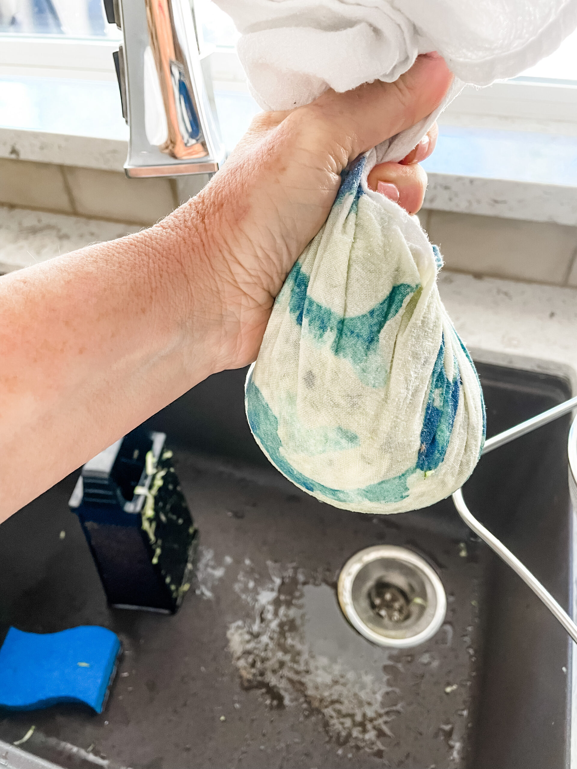 The raw shredded zucchini being squeezed out in a towel