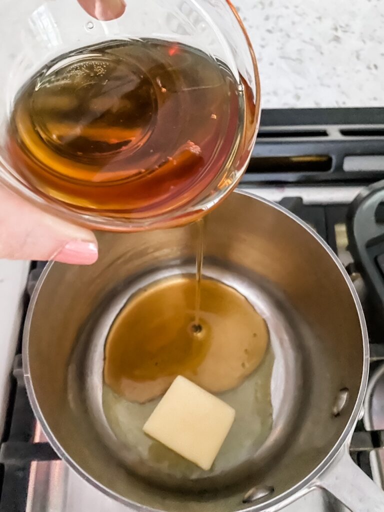 The maple syrup being poured into a saucepan with a knob of butter
