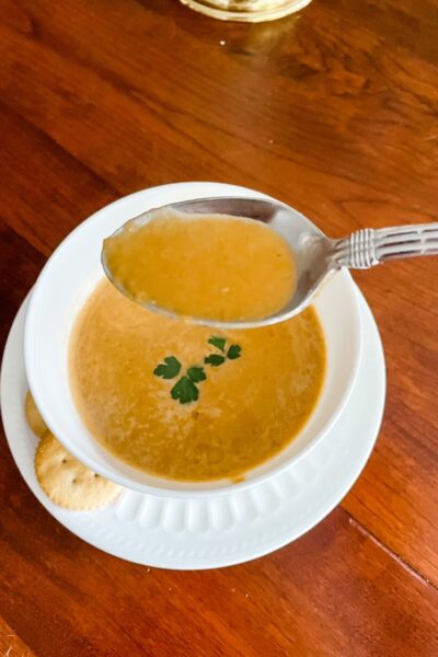 A spoon held above a bowl of Vegan Carrot and Red Lentil Soup