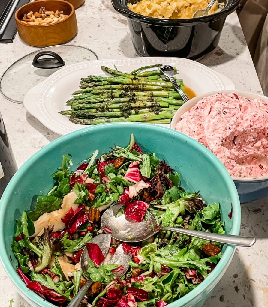 A bowl of the Chicory, Pear and Pomegranate Salad with Cranberry Vinaigrette next to other Thanksgiving entrees