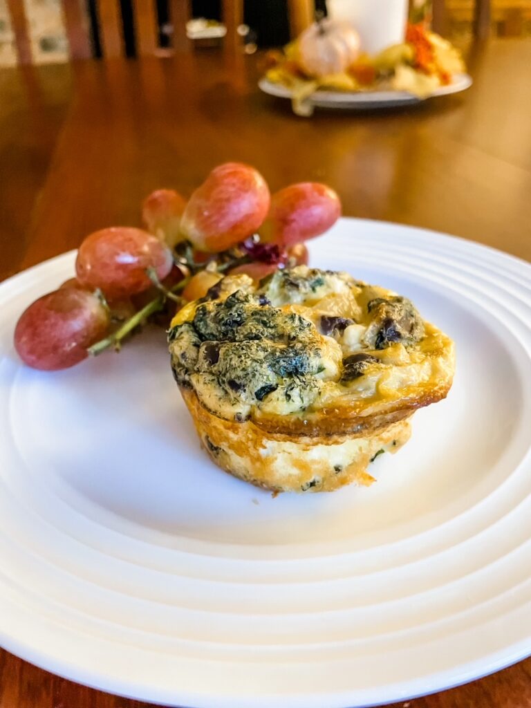 One of the finished Make Ahead Mediterranean Egg Cups on a plate with grapes