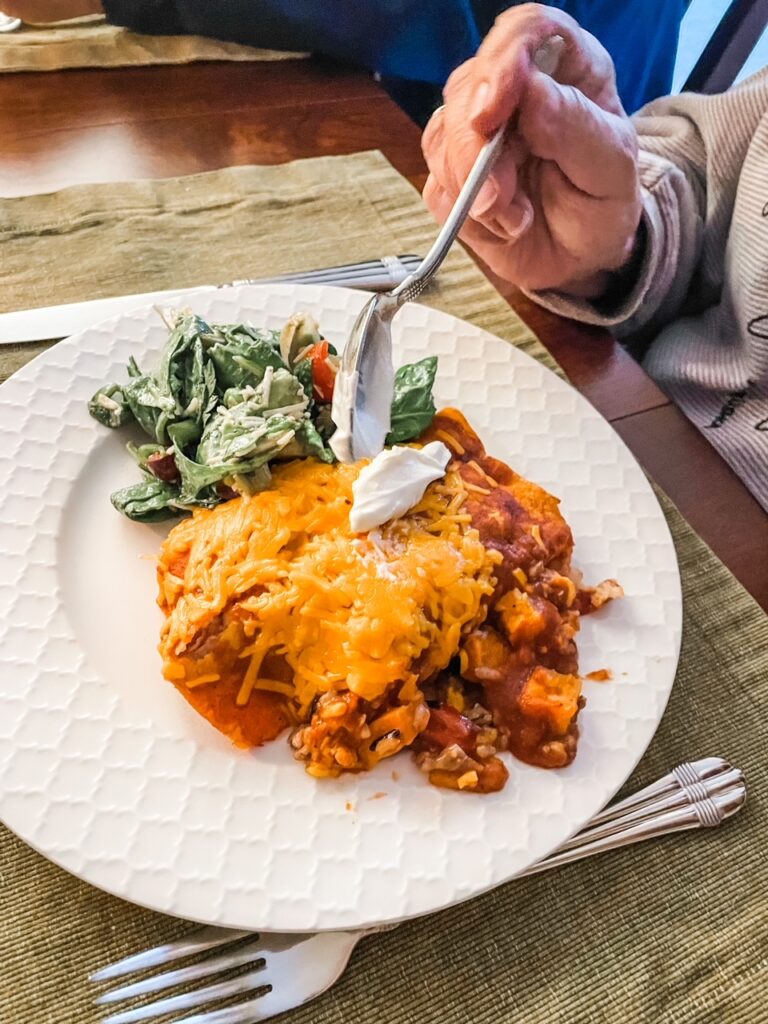 A portion of the enchiladas on a plate, with a person digging a fork into it