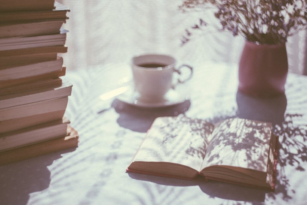 A stack of books, a open book, and a cup of tea