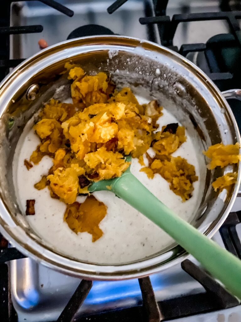 The roasted butternut squash being mixed into the cheese sauce