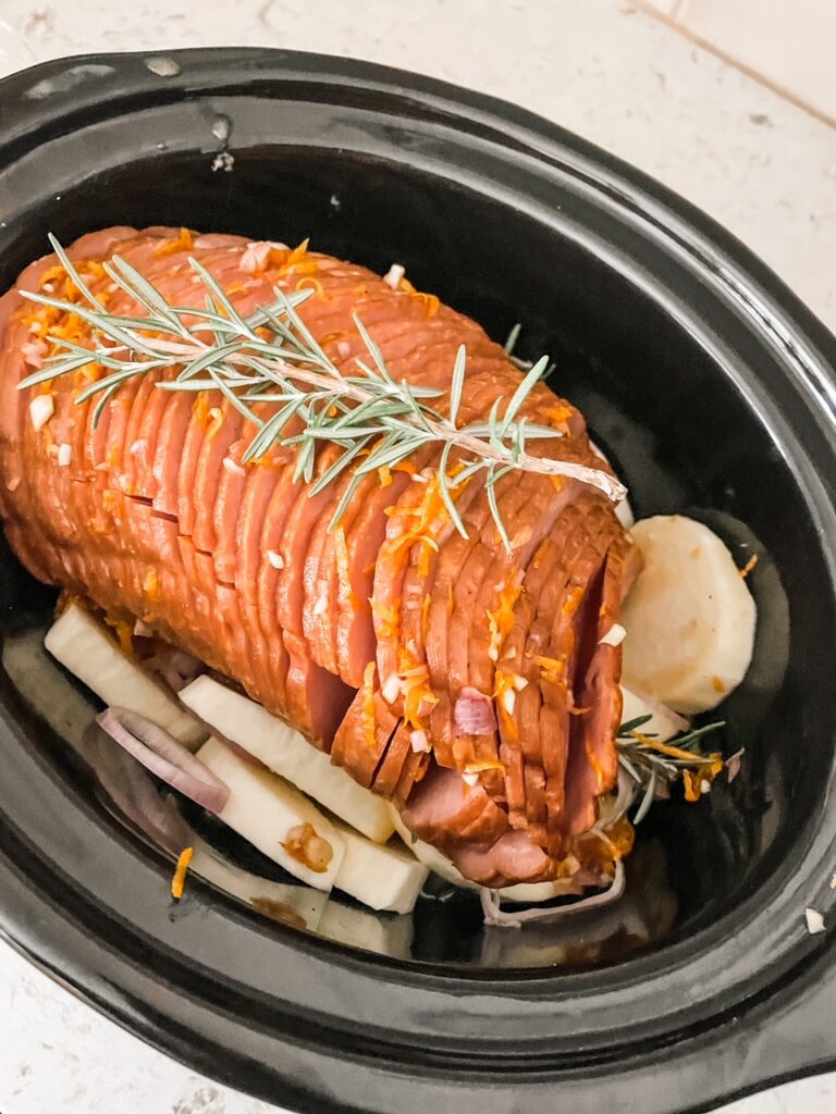 The ham, potatoes, thyme, and shallots in the slow cooker before cooking., with the orange sauce poured over the top of it