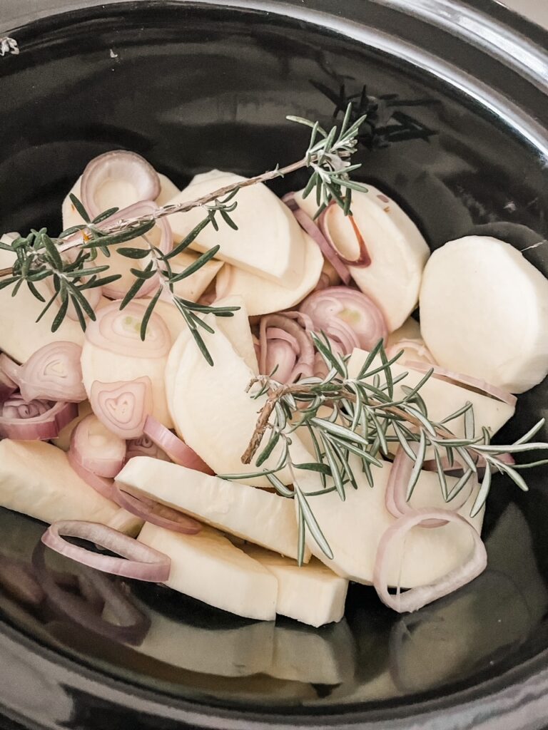 The ham, potatoes, thyme, and shallots in the slow cooker before cooking.