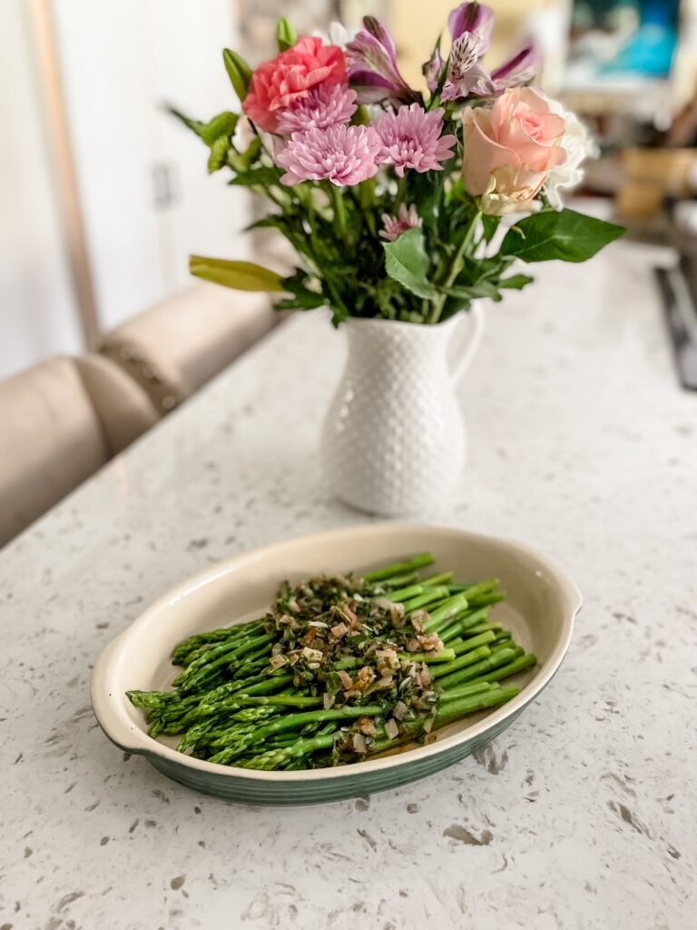 The plated Asparagus in Lemon Herb Vinaigrette with a bouquet of flowers in the background