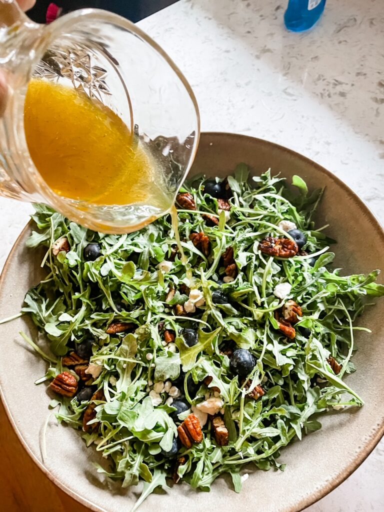 The dressing being poured into the Summer Arugula, Feta, and Blueberry Salad