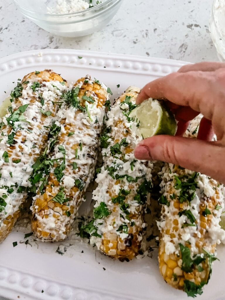 A lime wedge being squeezed over the finished Homemade Elotes or Mexican Street Corn