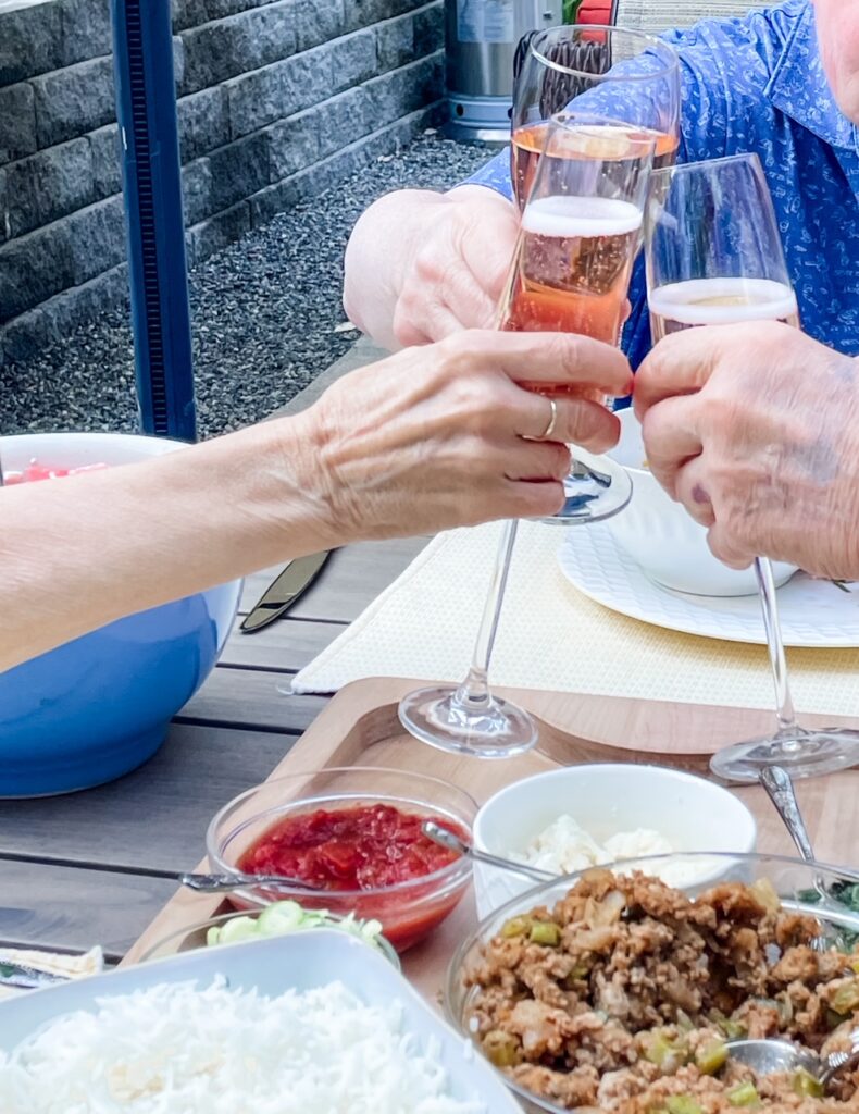 Two hands clinking glasses over a patio table