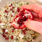 A pomegranate being held over the couscous dish