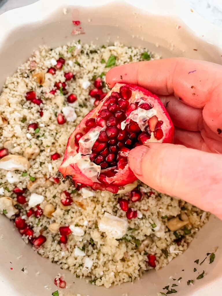 A pomegranate being held over the couscous dish