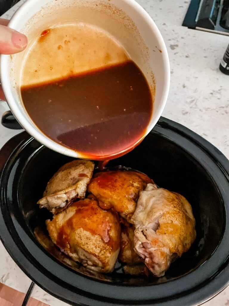 The sauce being poured over the chicken thighs in the slow cooker