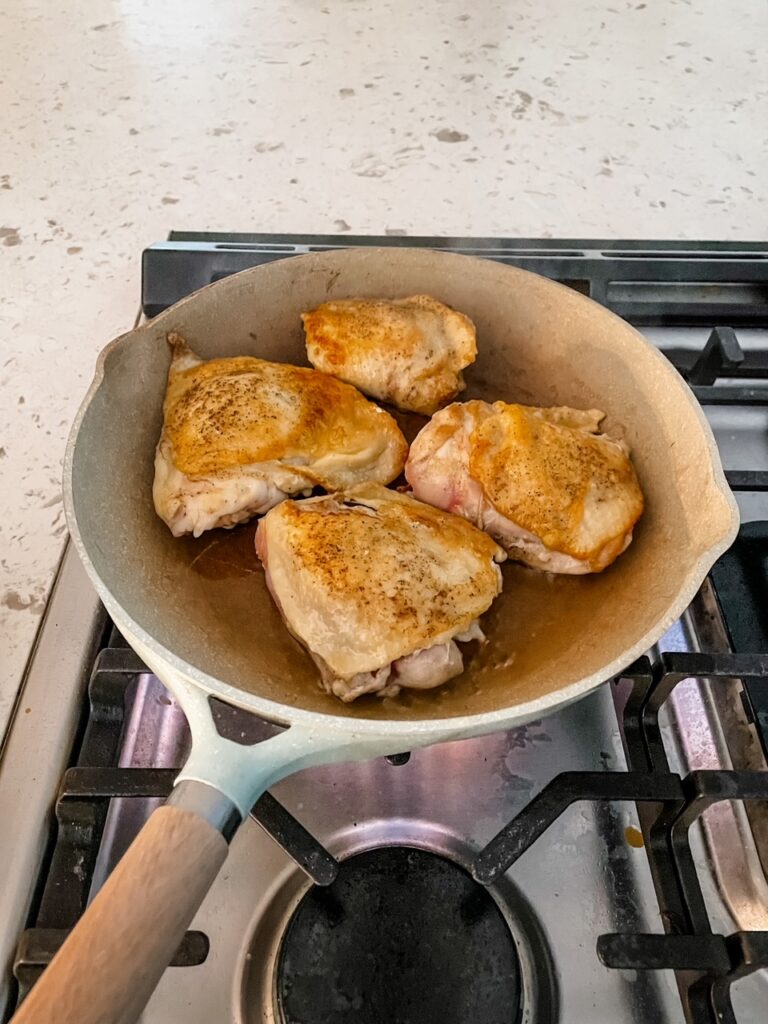 Four chicken thighs being seared in a pan