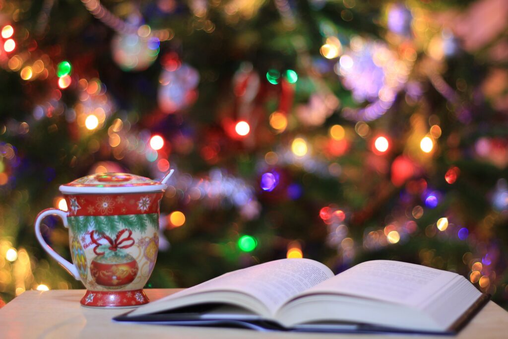 A book open in front of a Christmas tree and next to a mug for 2023 holiday reading