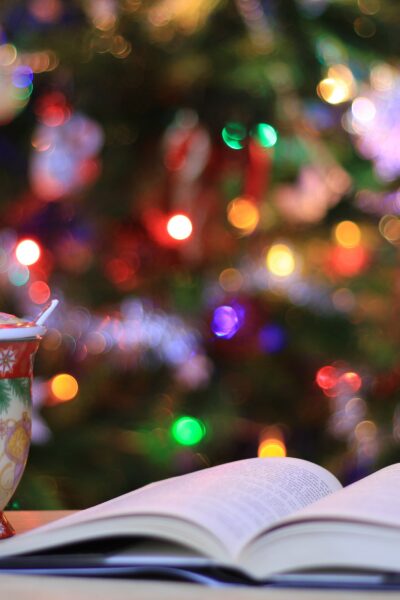 A book open in front of a Christmas tree and next to a mug