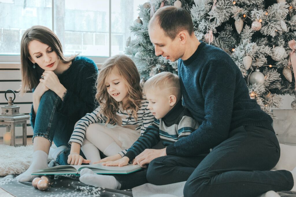 Parents 2023 holiday reading to their children in front of a Christmas tree