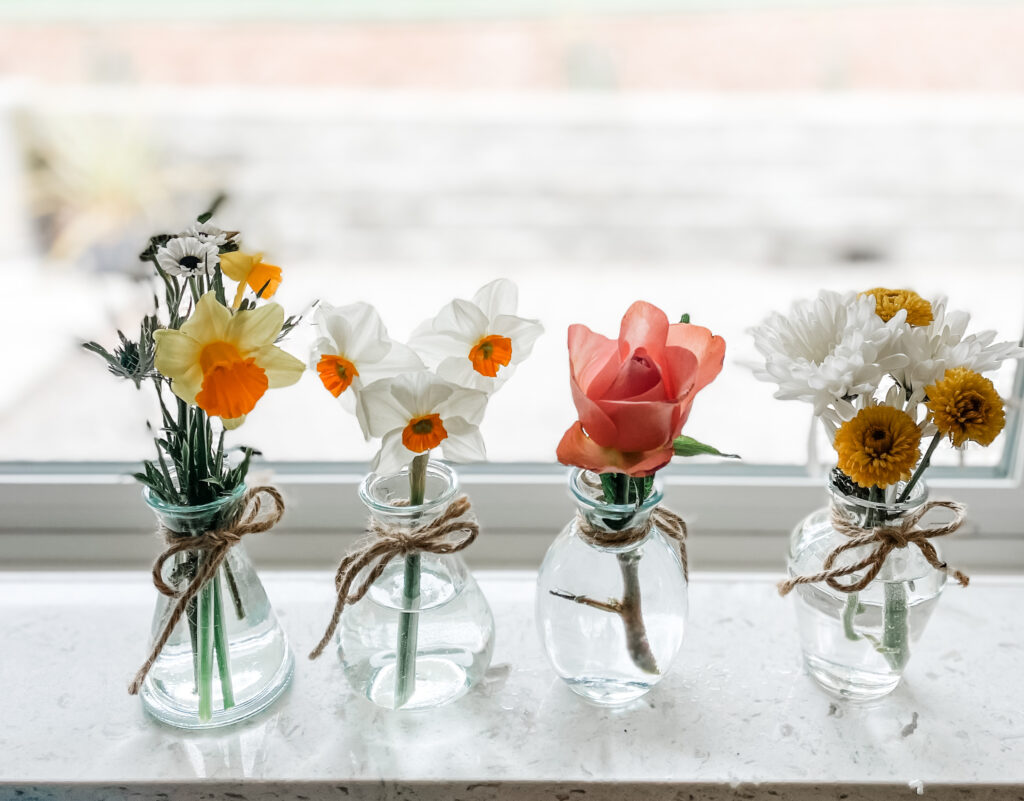 Photograph of four small glass vases with daffodils and pink roses.